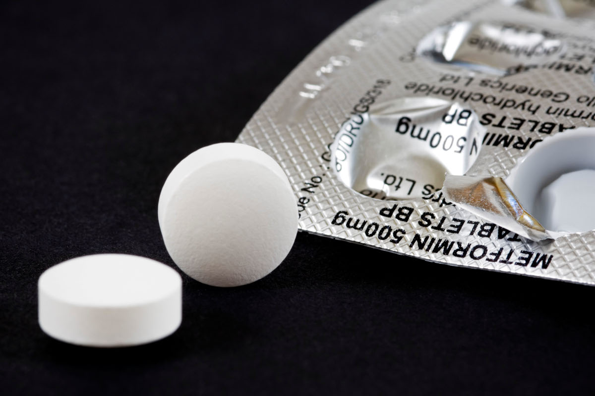 Horizontal macro close up of a blister pack of pills and two Metformin tablets on a black background