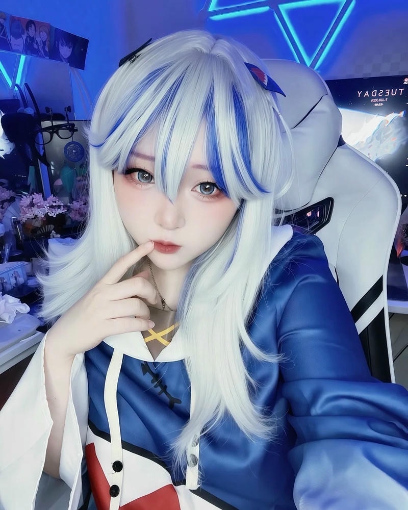 Nữ cosplayer gura ngồi trước máy tính phòng gaming màu xanh